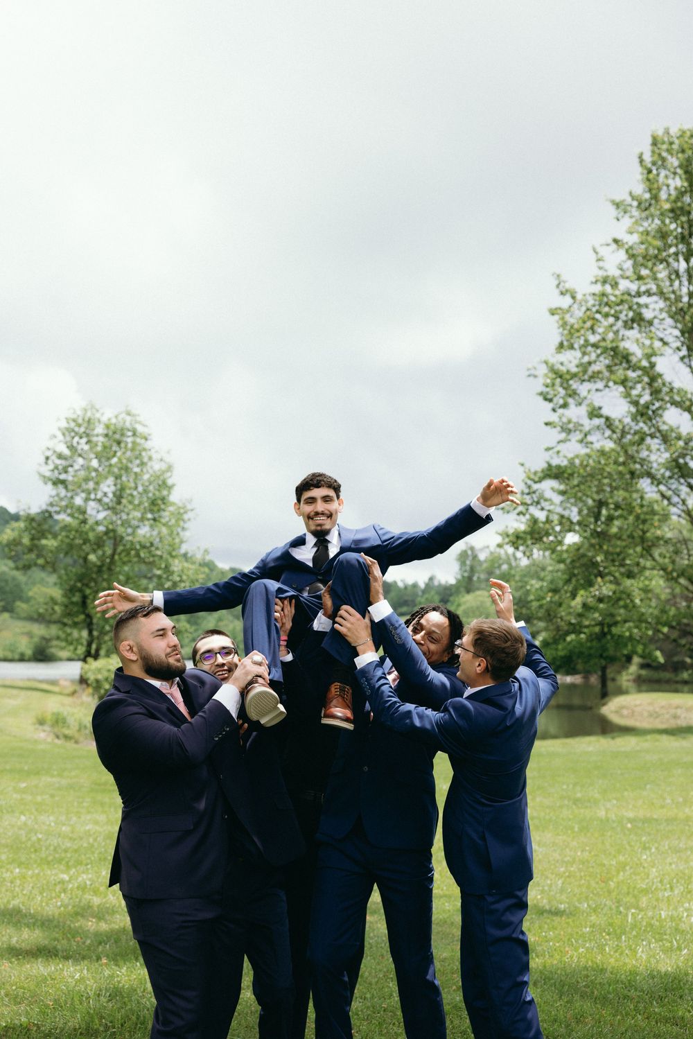 Groomsmen in navy suits celebrating and cheering together outdoors. Emotional documentary-style wedding photography