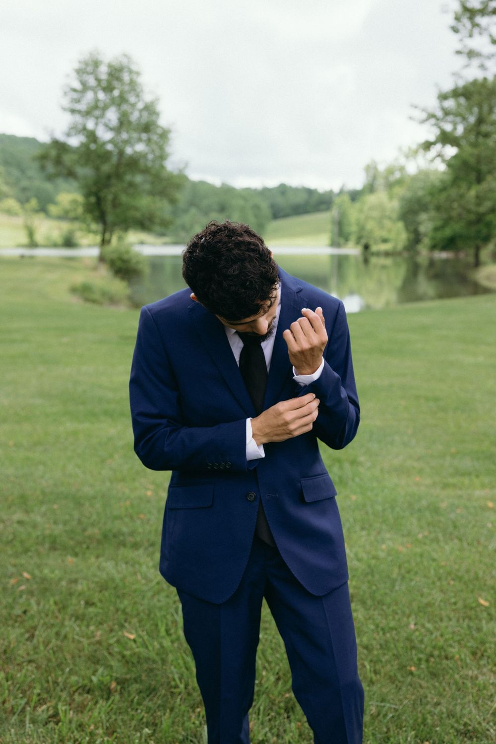 Groom in navy suit adjusting cufflinks outdoors. Estate and historic venue wedding photographer for NC and across the East Coast