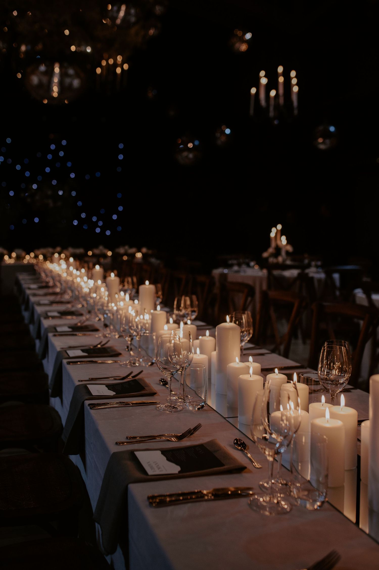 An elegant candlelit reception table with white linens and glassware creating a romantic ambiance.