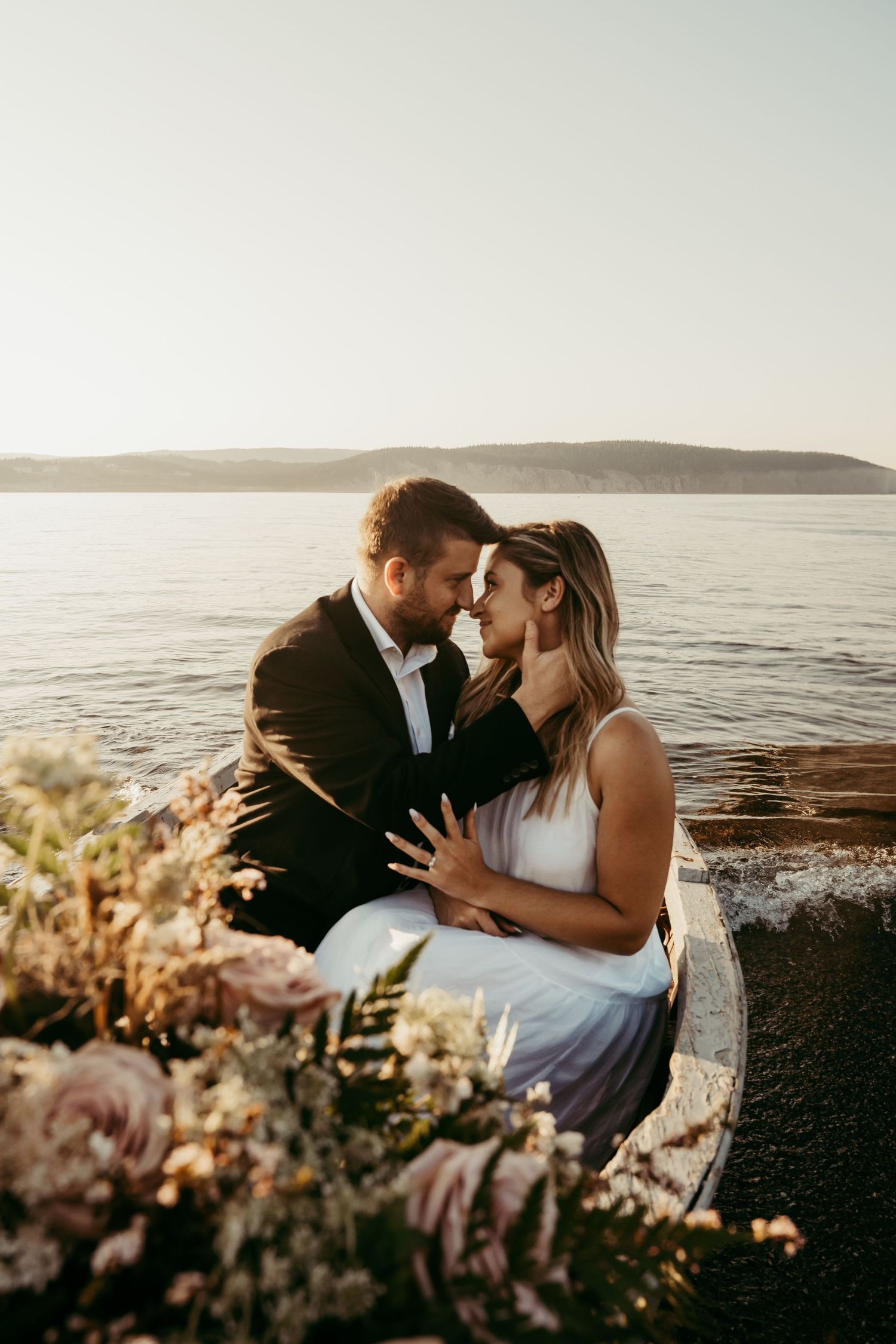Romantic couple sharing intimate moment by seaside with floral decorations at sunset.
