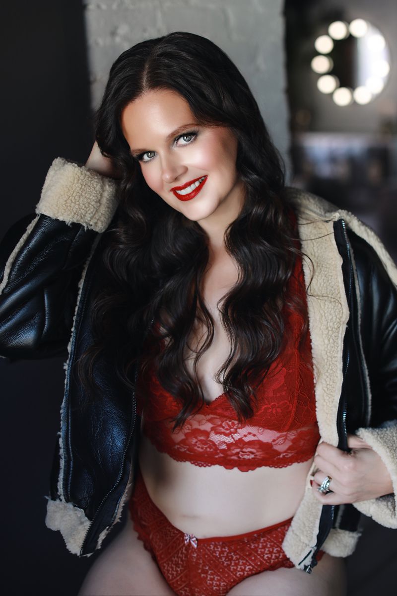 Fashionable winter look featuring a black shearling jacket and red lace lingerie set against blurred background lighting.
