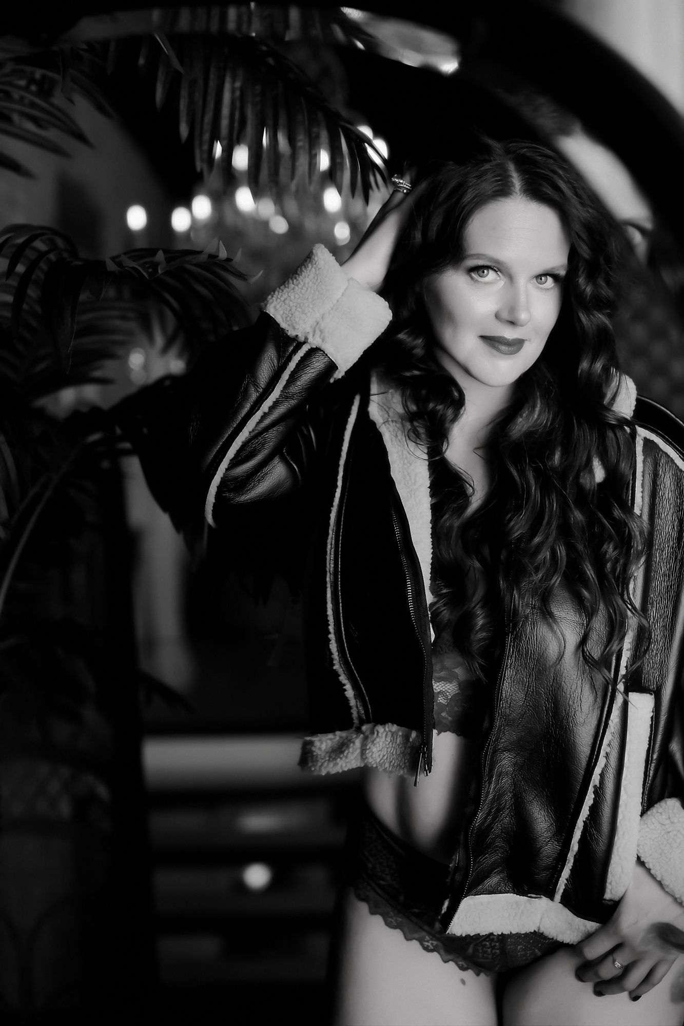 A black and white fashion portrait shows a woman in a leather jacket posing against a background with blurred lights.