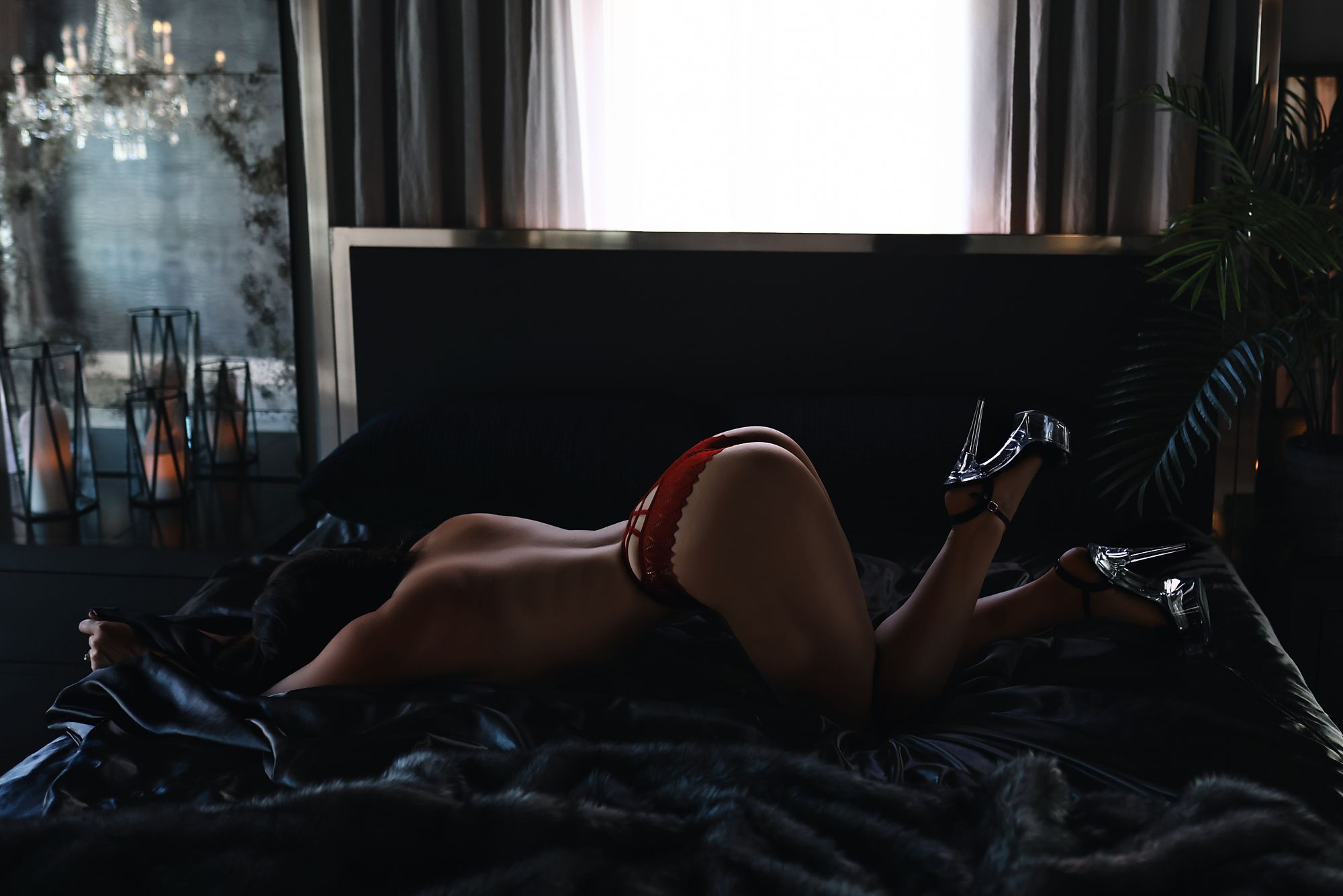 Silhouette of someone in lingerie lying on dark bedding in a moody, dimly lit bedroom interior.