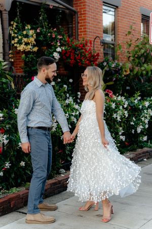 A romantic couple poses in front of a floral garden wall, with the bride wearing a stunning white dress.