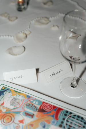 Place cards and wine glass on white tablecloth with decorative pattern.