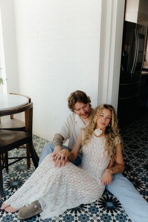 Couple sitting on patterned tile floor in casual white outfits.