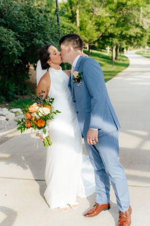 A tender wedding moment captured outdoors with a colorful bouquet and light blue suit.