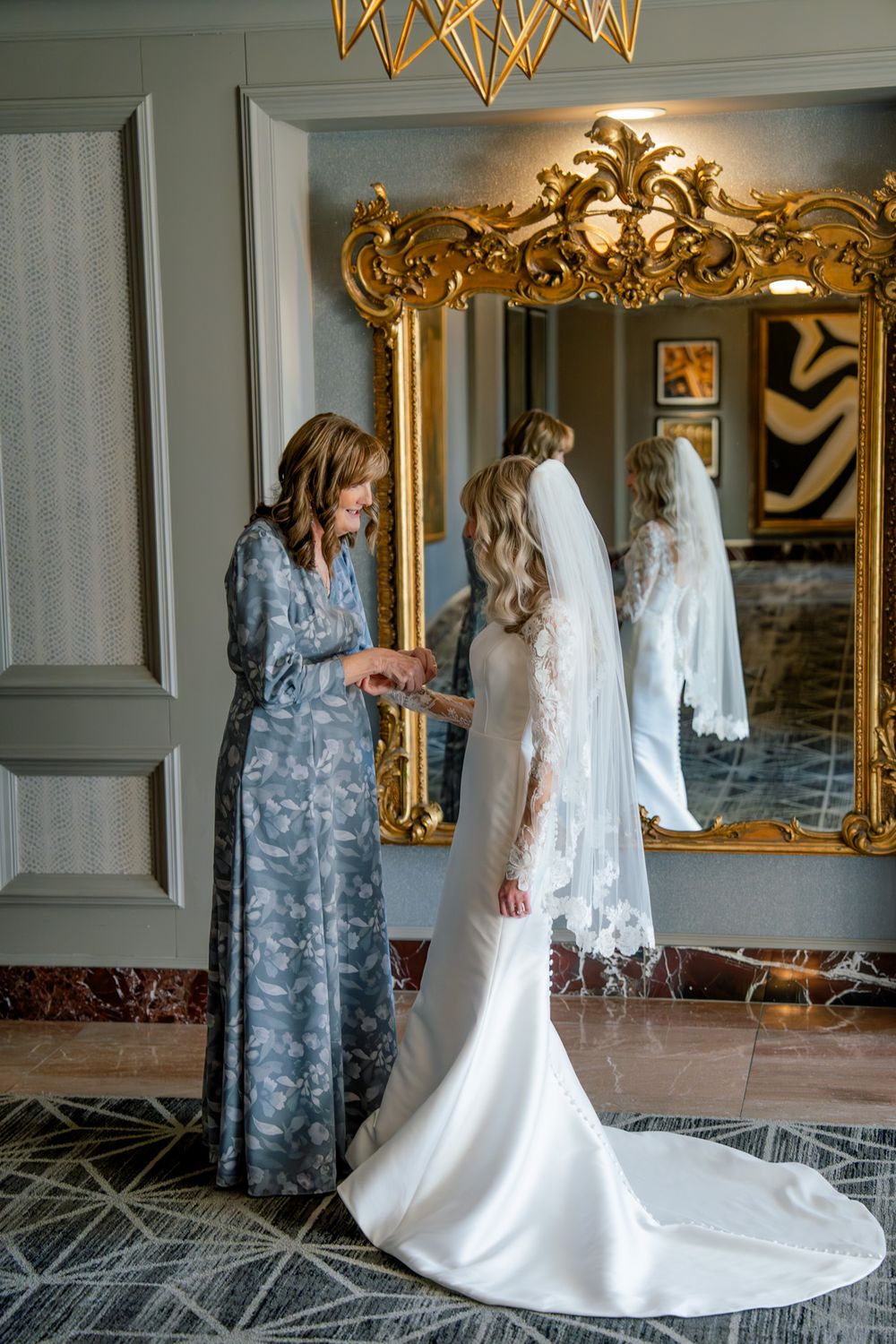Final wedding dress preparations in an elegant room with ornate gold mirror.