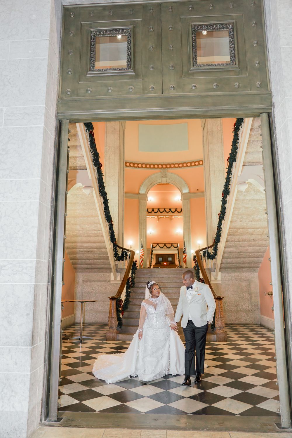 Wedding couple framed in doorway of elegant building with checkered floor.