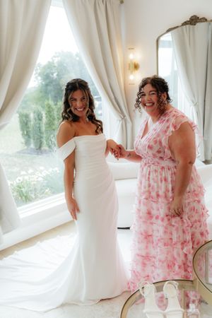 A sunlit bridal preparation moment with elegant white and pink dresses in a bright room.