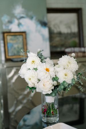 Elegant white floral arrangement with roses and daisies in clear glass vase.