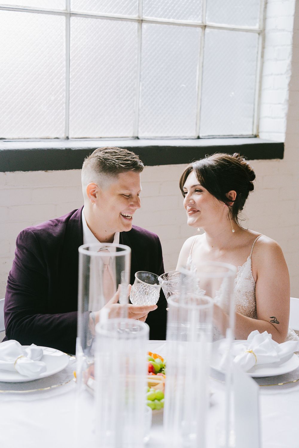 Couple sharing intimate moment at wedding reception table with glassware.