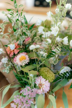A delicate floral arrangement featuring pink, white and orange blooms with green foliage in soft natural light.