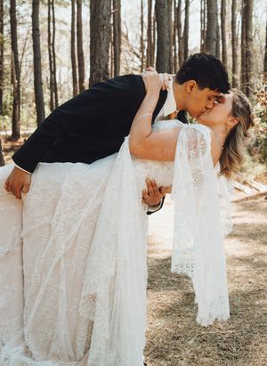 Romantic dip kiss portrait in a sunny forest setting.