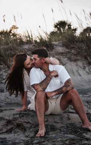 A romantic couple embracing and kissing on a sandy beach at sunset.