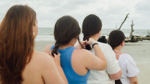 A group of people stand in a row on a beach looking out towards the ocean during sunset.