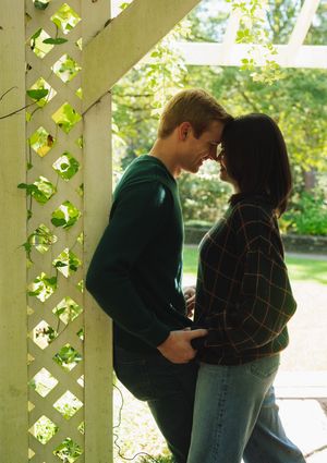 A couple shares an intimate moment on a porch with lattice and greenery in the background.