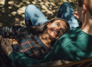 Person lying on ground in dappled sunlight wearing a green sweater and dark hair.