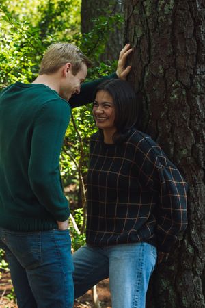 Two people share a moment together while standing by a large tree trunk in a sunny outdoor setting.