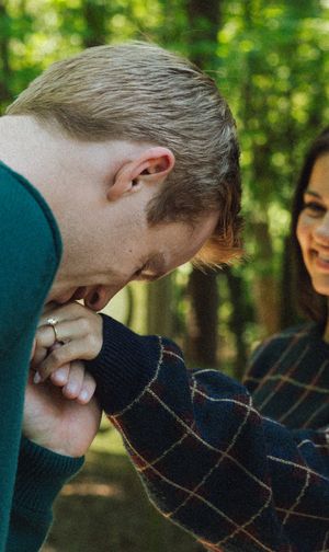 A couple sharing a joyful moment together in a sunlit forest setting.