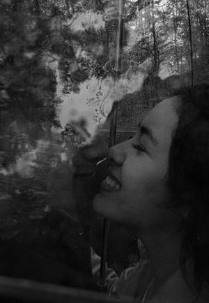 Artistic black and white portrait of person smiling against forest background.