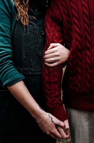 Close-up of two people holding hands wearing denim overalls and a red knit sweater.