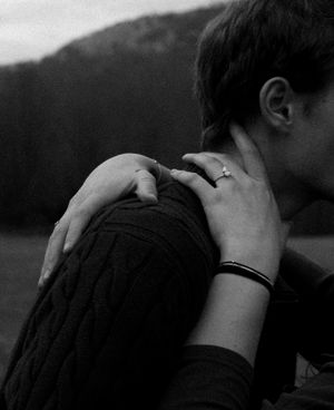 Intimate black and white photo of two people embracing with focus on hands and shoulders.