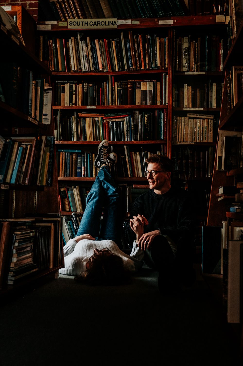 Intimate engagement photos in a cozy library surrounded by walls of books.