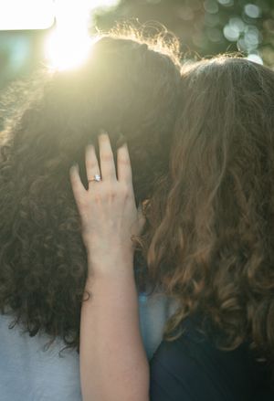 A hand reaches up to touch curly brown hair with sunlight creating a soft bokeh effect in the background.