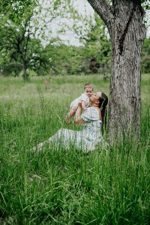 Couple sharing an intimate moment by a large tree trunk in tall summer grass.