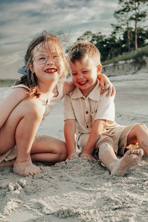 Children playing and laughing together on a sandy beach with cloudy skies in the background.