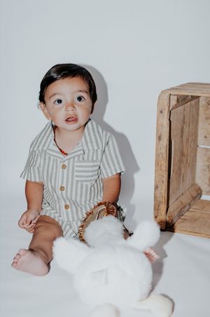 Baby wearing striped button-up outfit sitting next to wooden crate with white plush toy.
