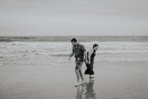 Two people walking along a misty beach shoreline in black and white photography.