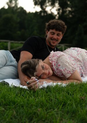A couple lies together peacefully on green grass during a romantic outdoor photoshoot at sunset.