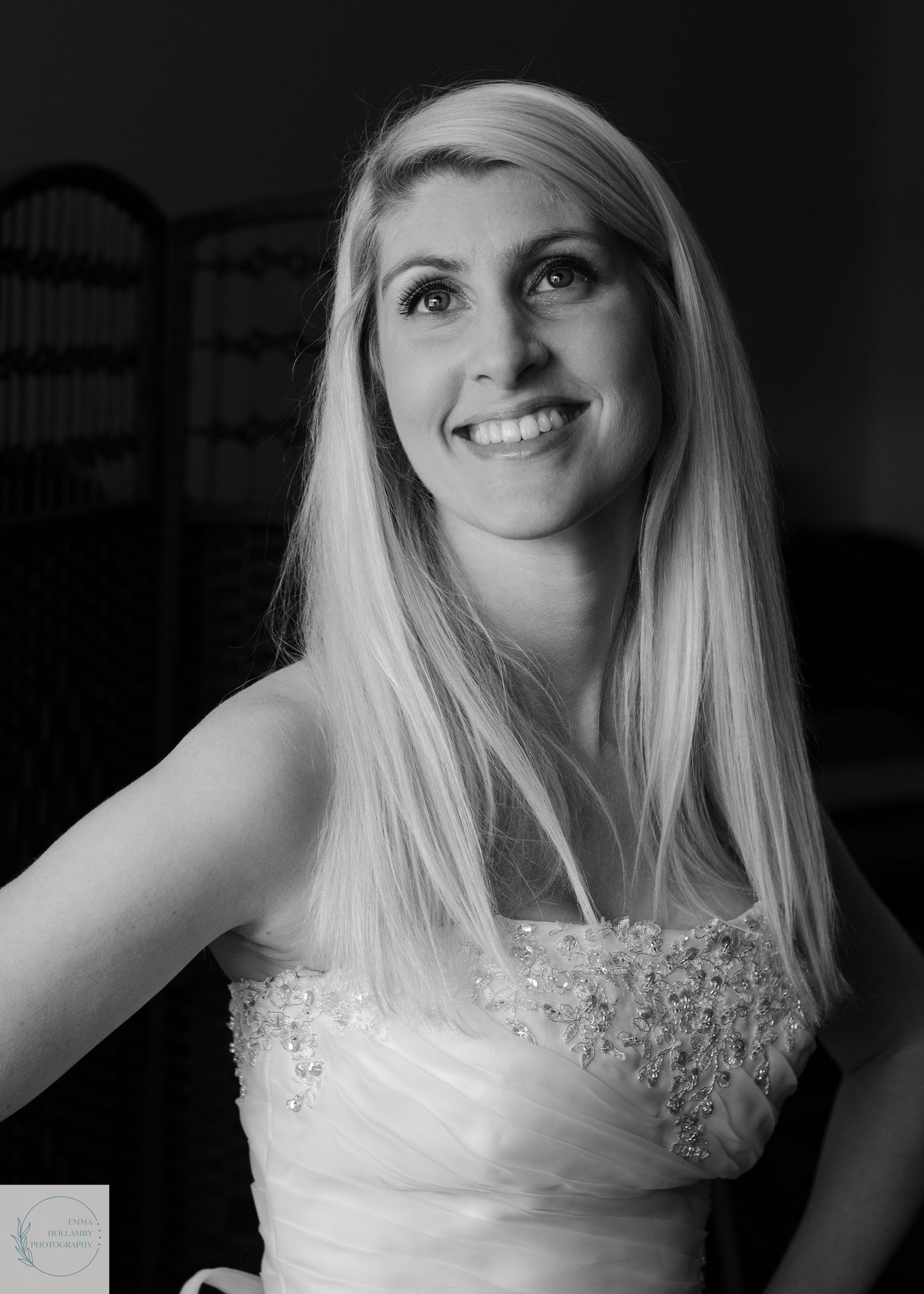 Black and white portrait of a blonde bride in a beaded strapless wedding gown smiling radiantly.