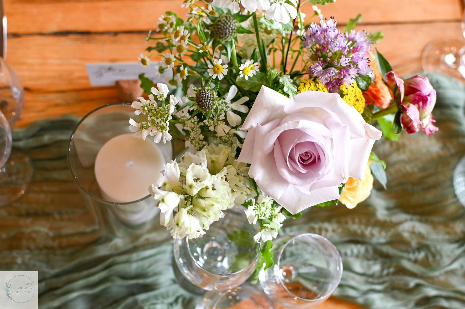 Elegant wedding table centerpiece with pink roses and wildflowers in glass vases with candle.