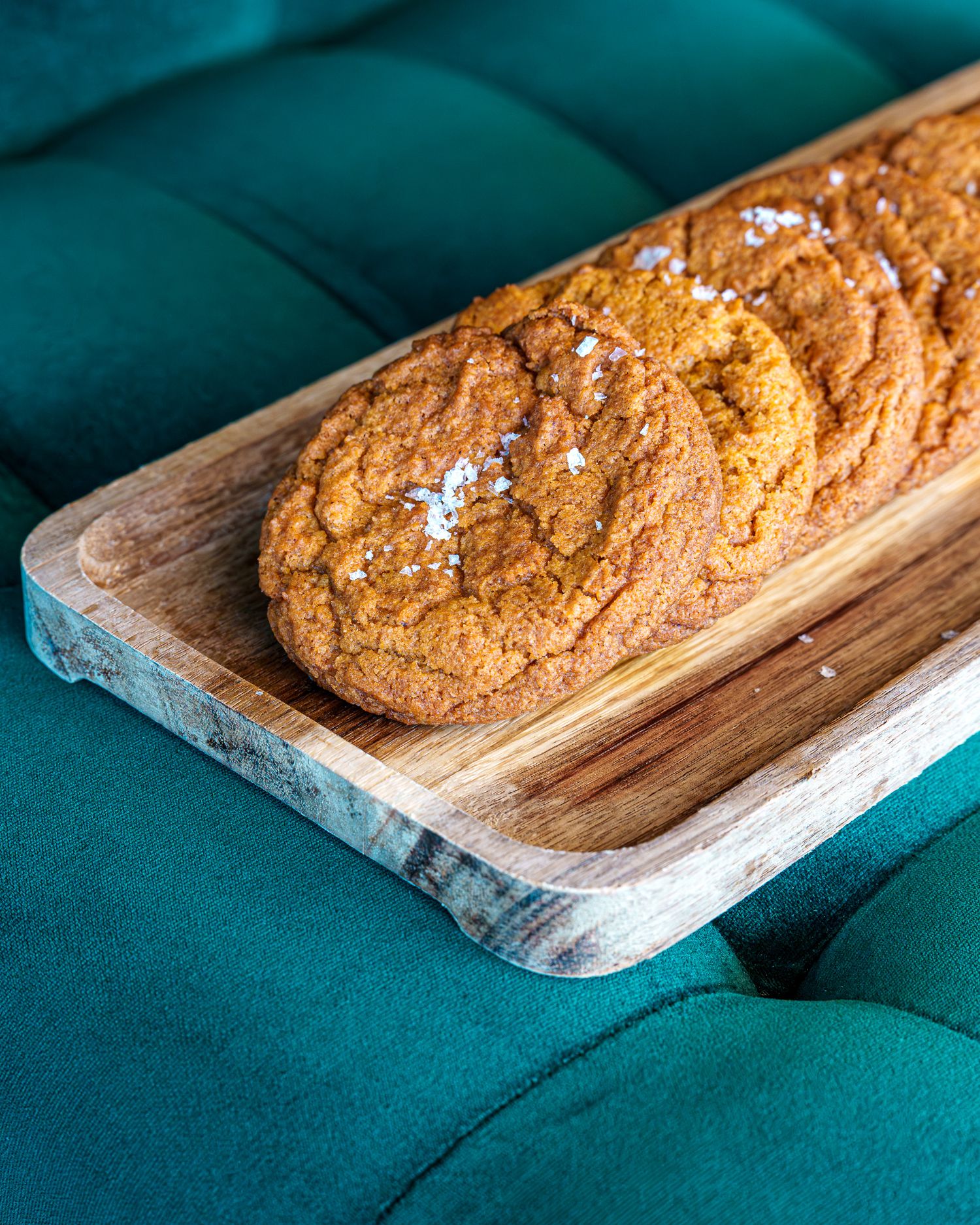 Susana Querejazu pumpkin cookies with sea salt flakes rest on a rustic wooden serving board against a teal velvet background.