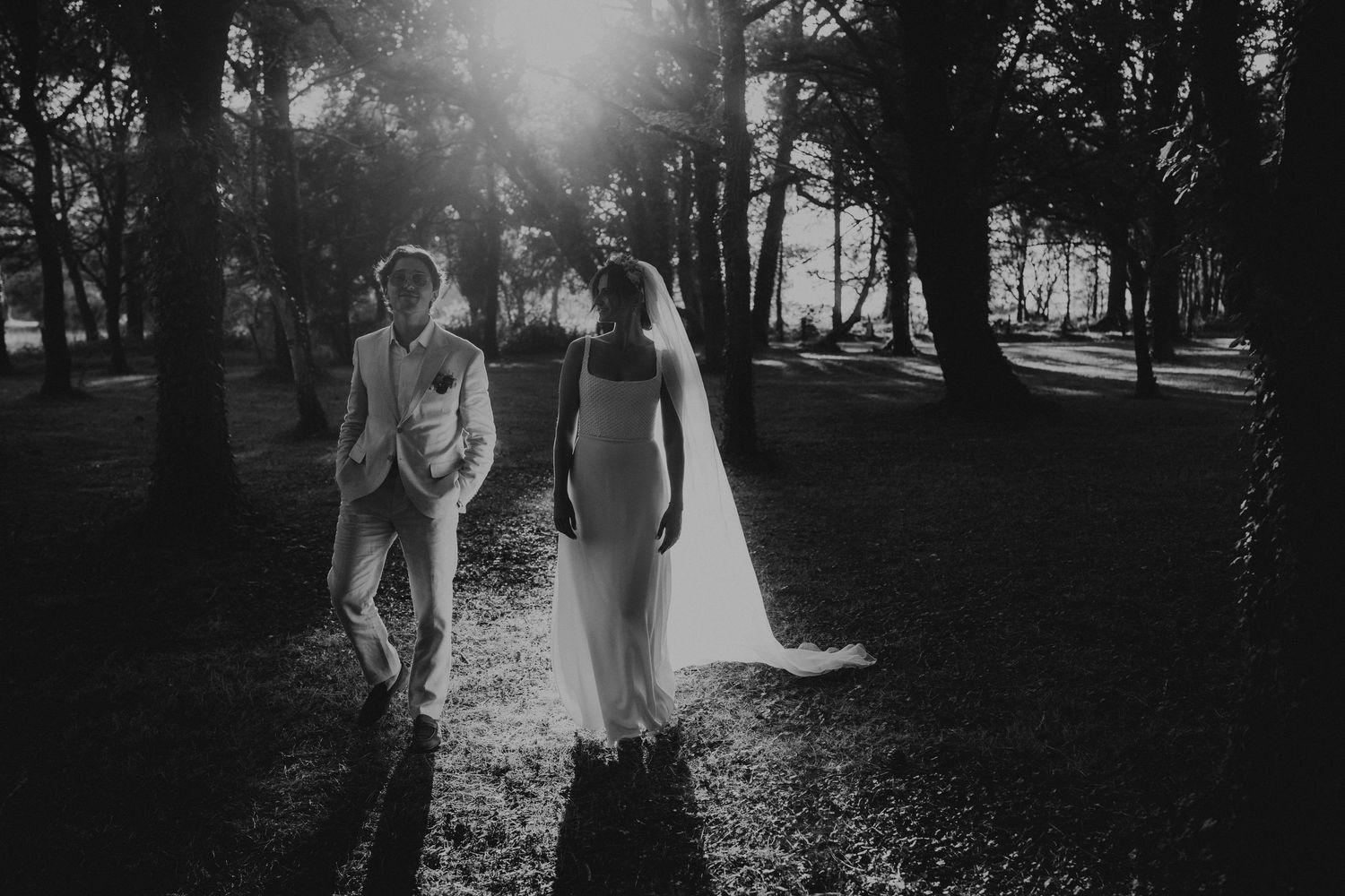 A romantic black and white wedding photograph showing a tender embrace in a natural outdoor setting.