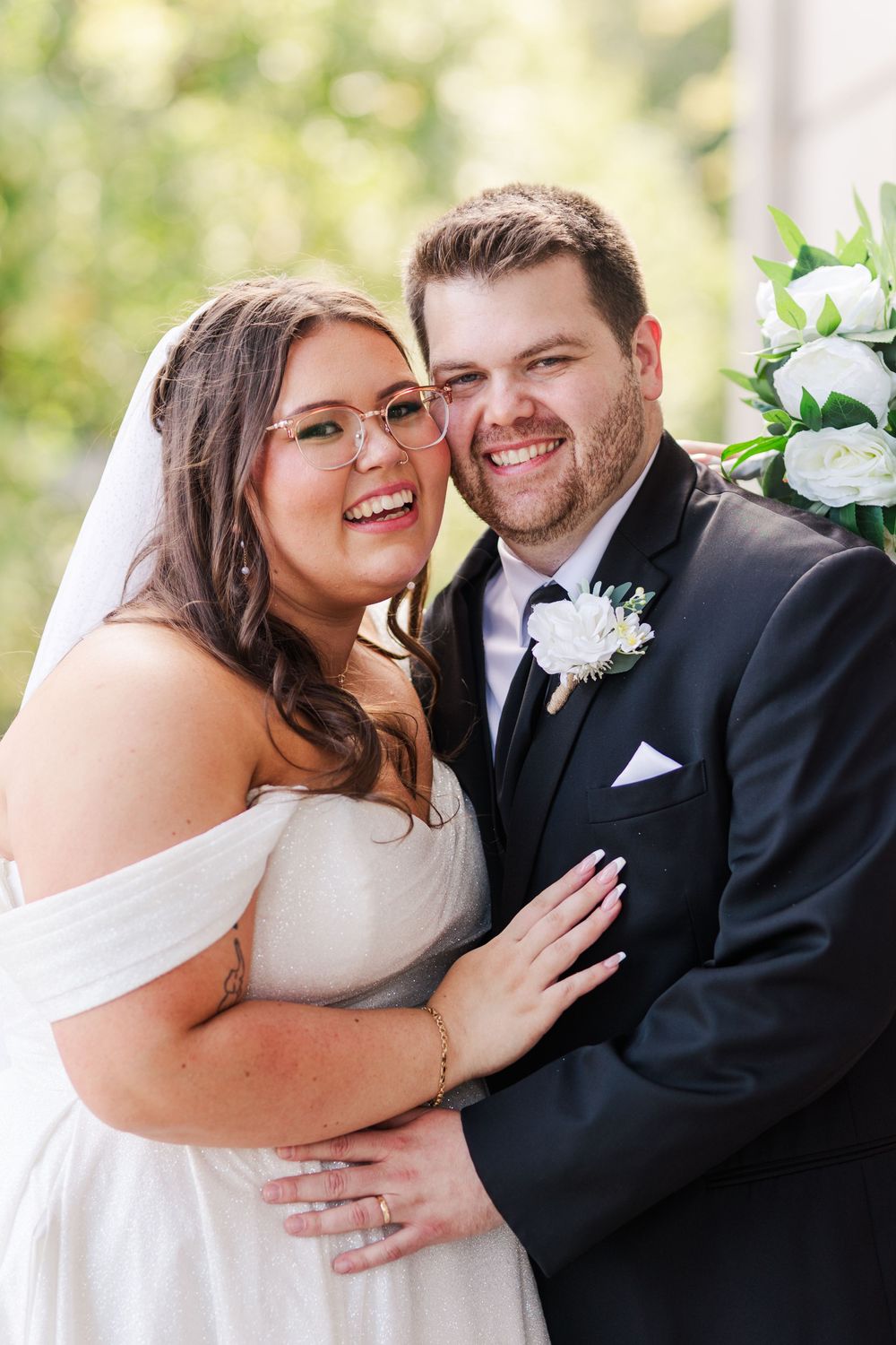 Happy couple shares intimate moments in formal wedding attire with white floral decor in background.