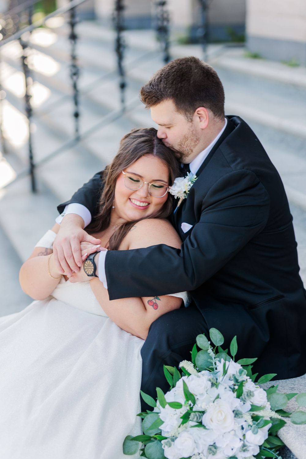 Happy newlyweds share intimate romantic moments together during wedding portraits with white bridal bouquet.