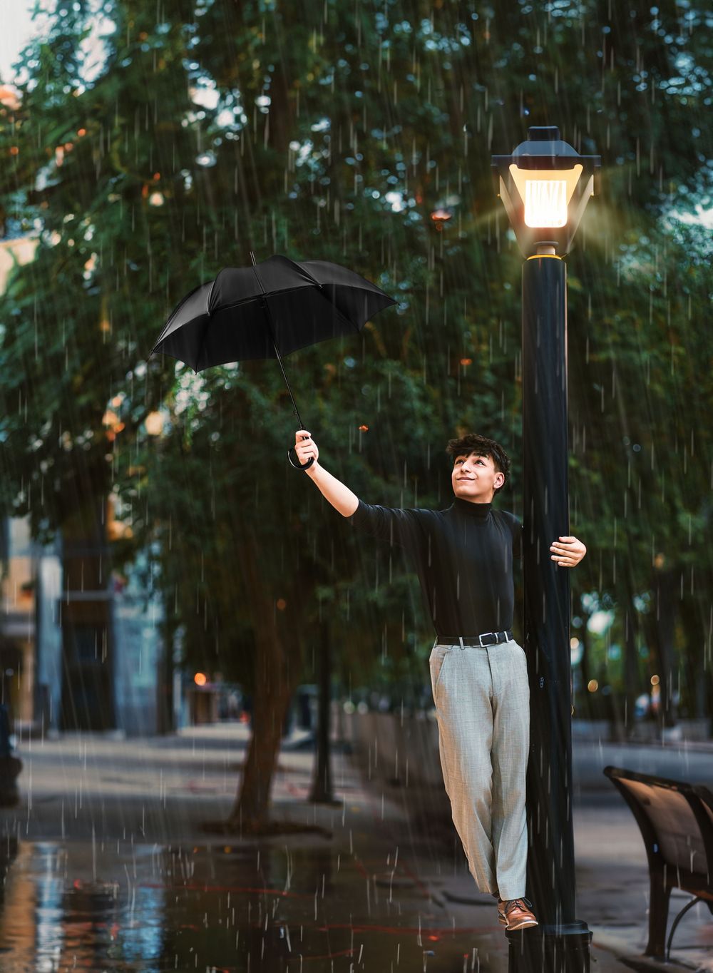 Young man dancing in rain holding umbrella beside glowing street lamp in cinematic outdoor portrait.