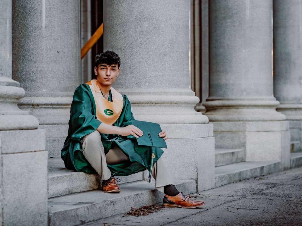 Graduate in green robe and gold medallion sitting on stone steps between classical columns.