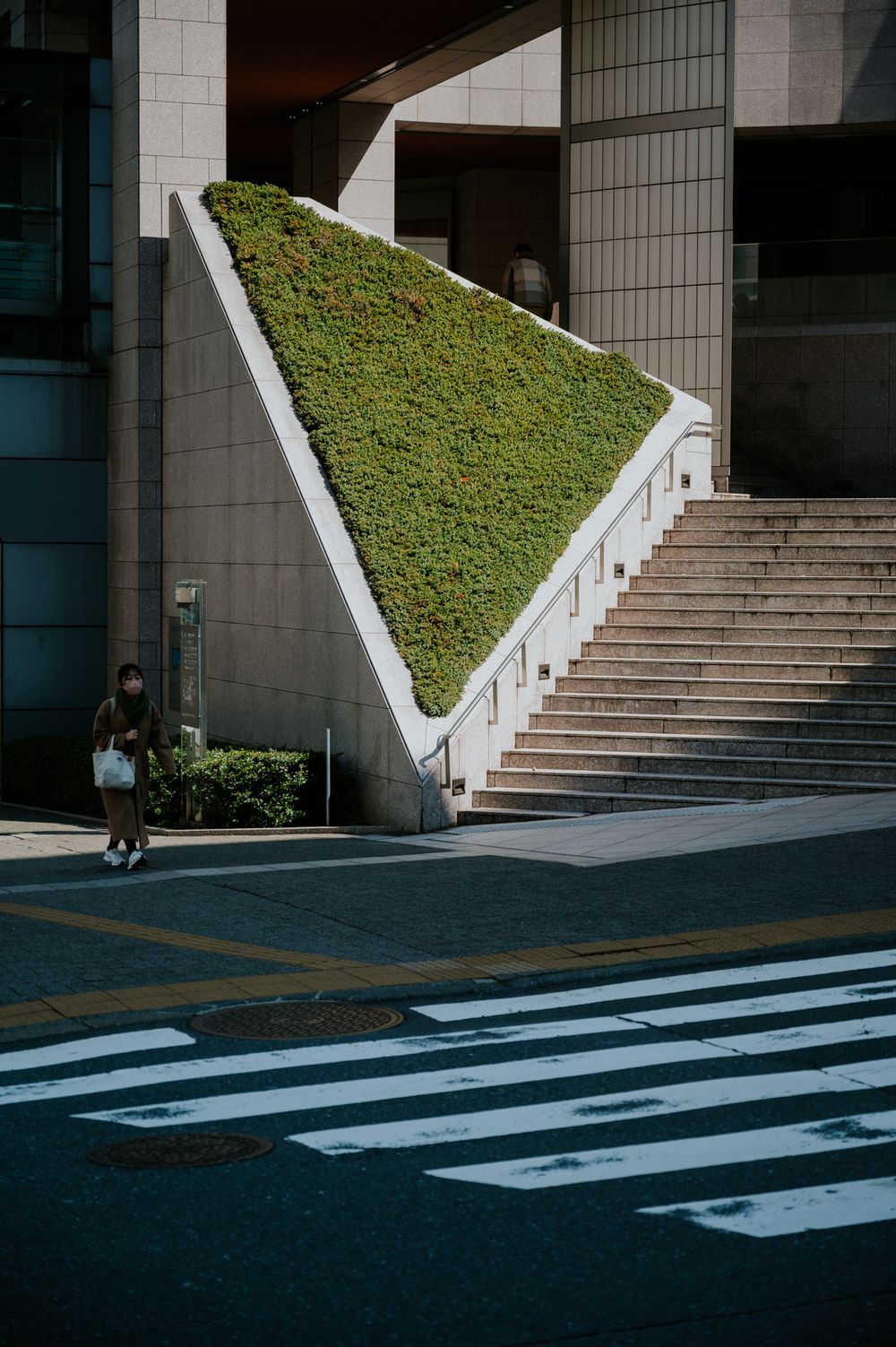 Modern building entrance with white stairs, grass landscaping, and crosswalk stripes on the pavement.