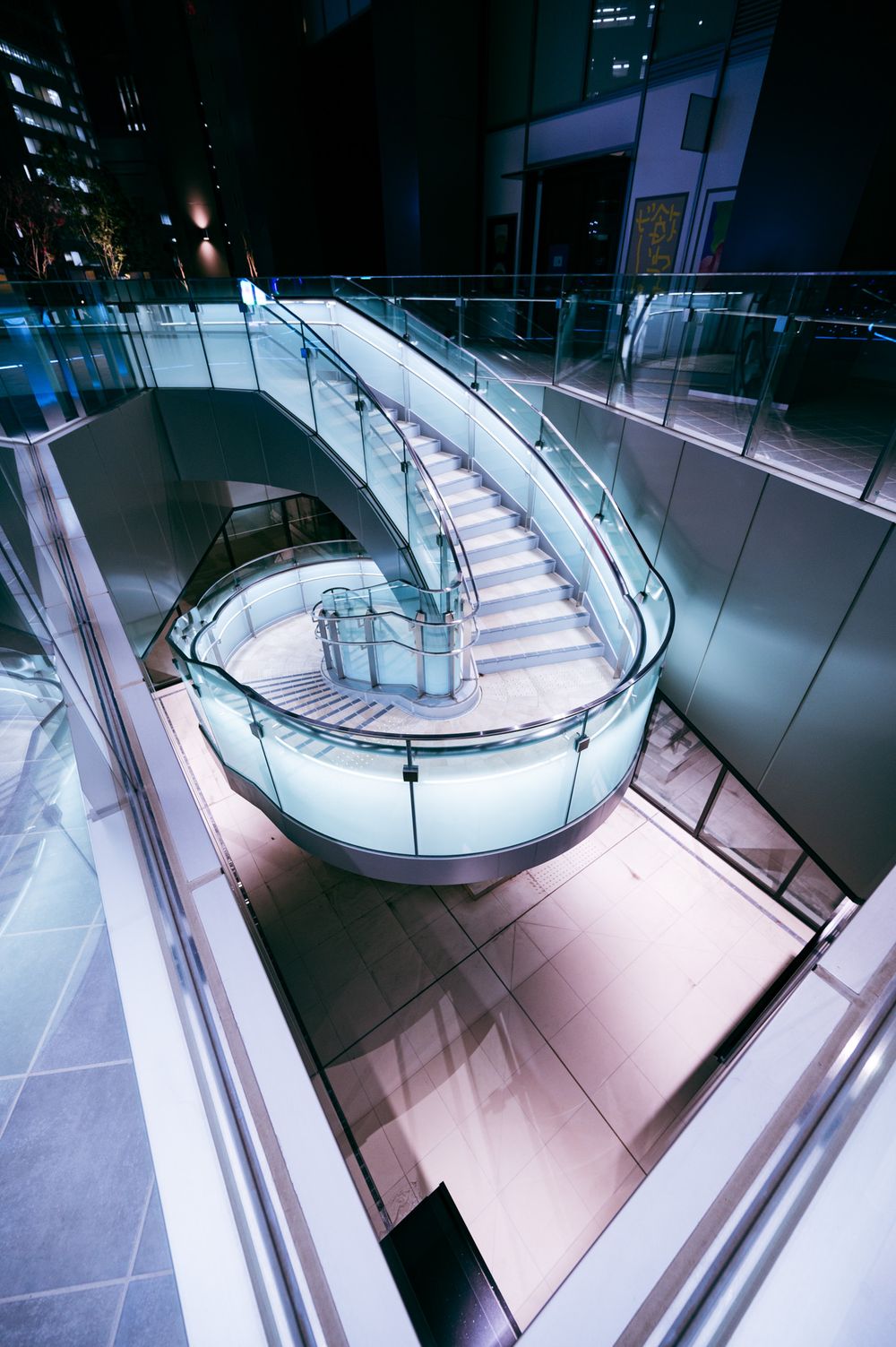 Modern spiral staircase with illuminated white steps curves upward in a minimalist interior space.