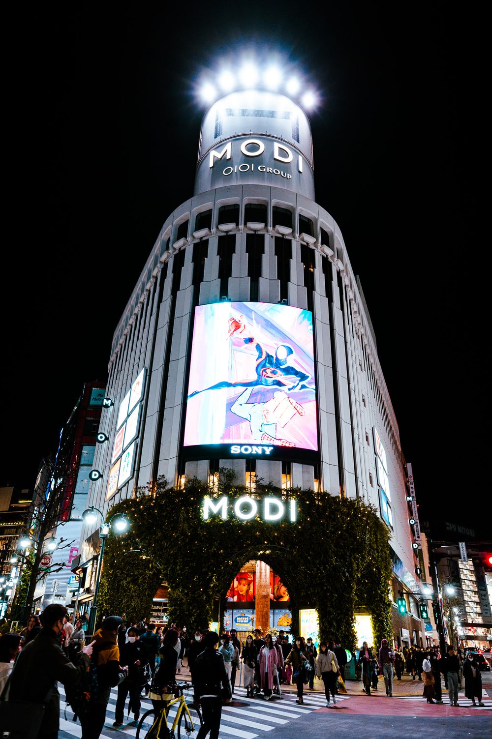 The iconic Shibuya Modi building illuminated at night with bright electronic displays in Tokyo's bustling shopping district.