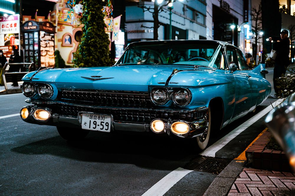 Vintage blue classic Cadillac with chrome trim parked on a city street at dusk.