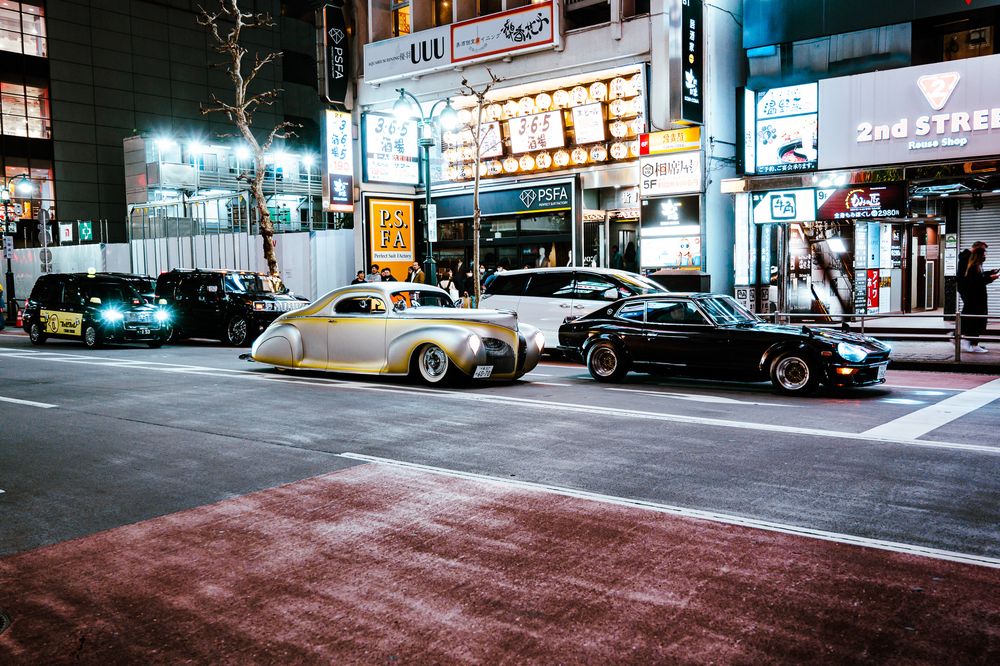 Empty urban street at night illuminated by neon signs and storefront lights.