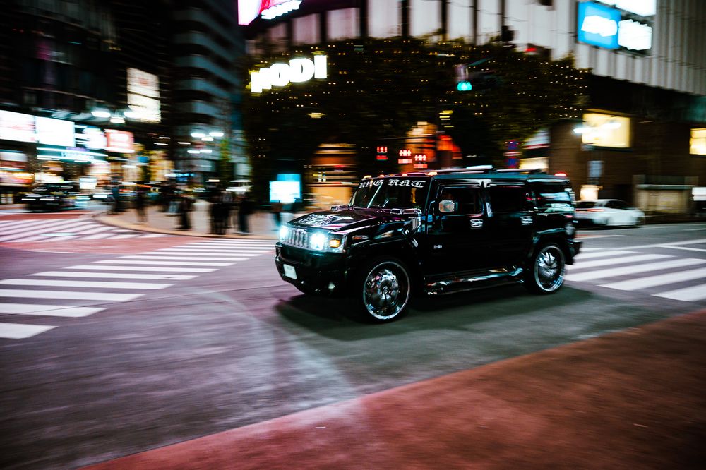 Nighttime city street with cars and neon lights reflecting off wet pavement.