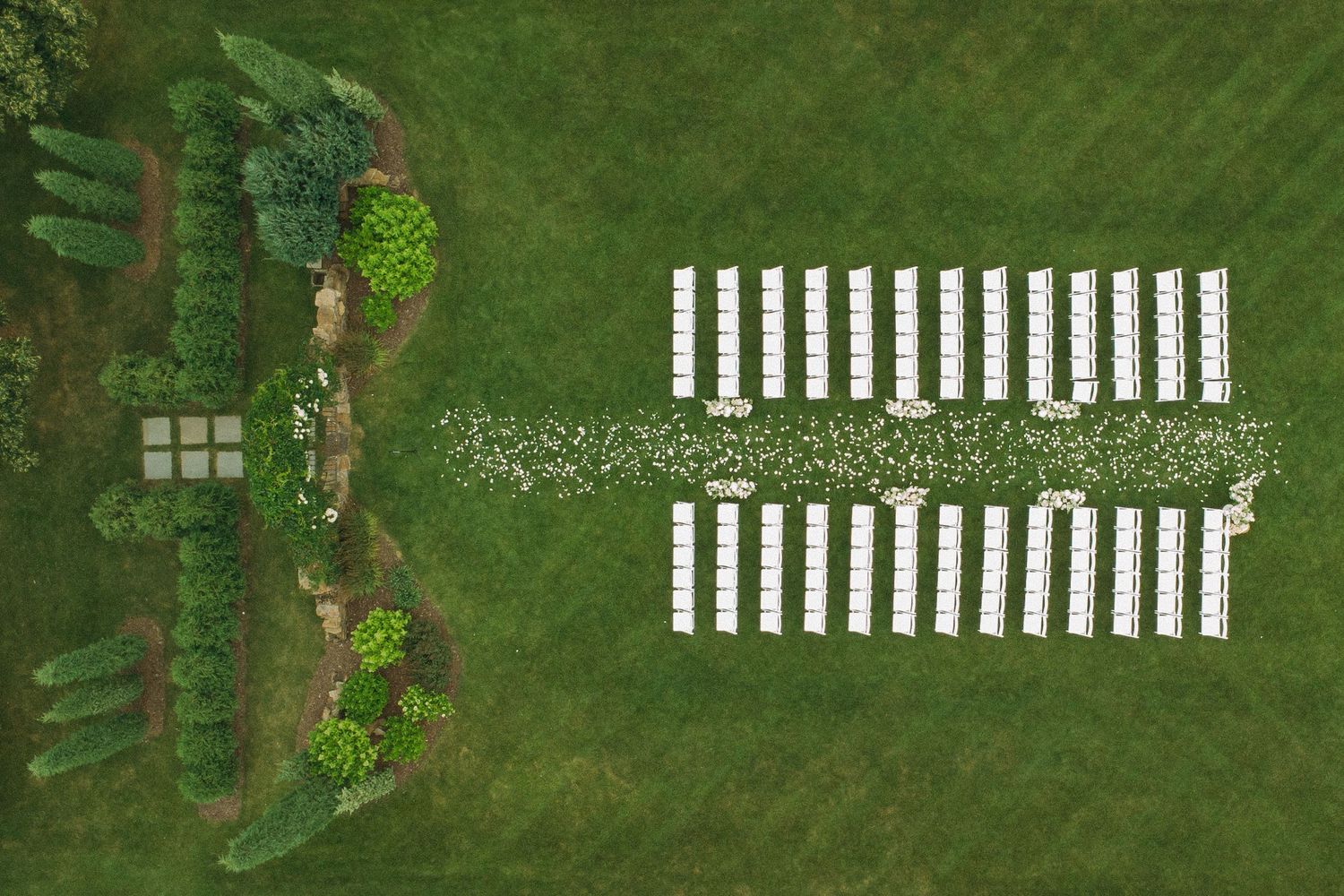 Aerial view of white chairs arranged in rows on manicured green lawn for outdoor wedding.