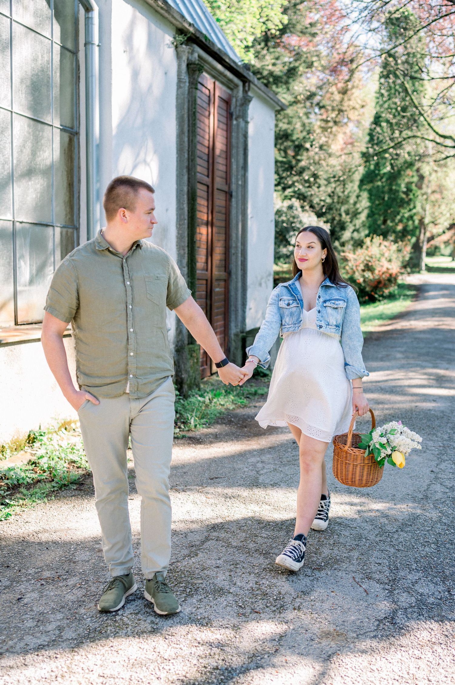Couple holding hands while walking on sunny path with wicker basket.